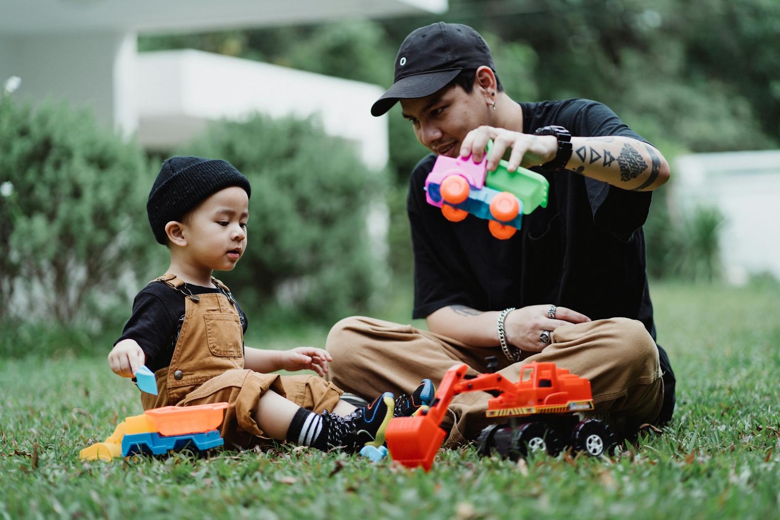 Father and son bonding over toy trucks on a grassy yard. Capturing moments of play and parenting.