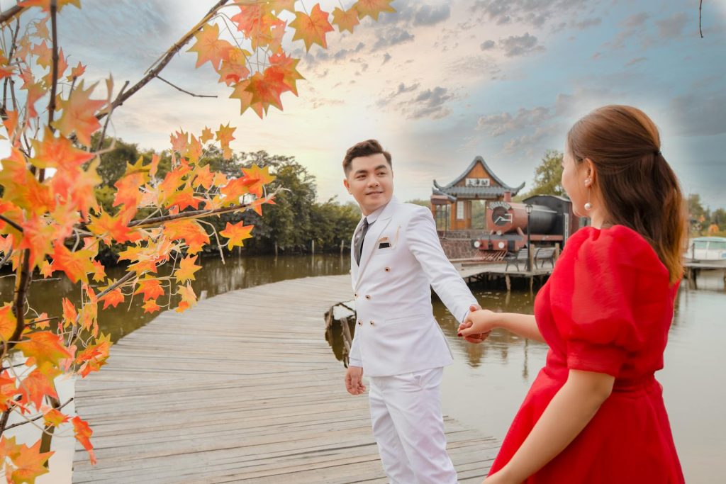 Couple holding hands on a wooden dock with vibrant autumn leaves and serene lake view.